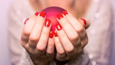 Mãos de uma mulher segurando uma esfera vermelha com unhas pintadas de esmalte vermelho vivo.
