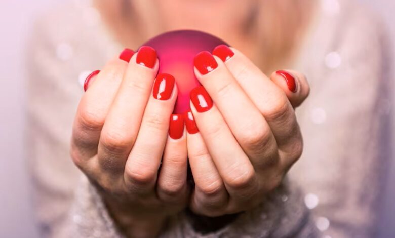 Mãos de uma mulher segurando uma esfera vermelha com unhas pintadas de esmalte vermelho vivo.
