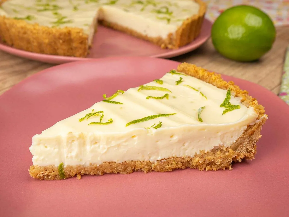 Fatia de torta mousse de limão, com raspas de limão por cima, em prato rosa. Sobremesa popular no Brasil, feita com mousse de limão e crosta de biscoito."