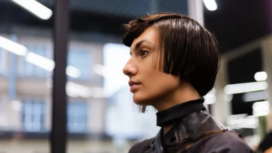 Mulher com corte de cabelo curto em estilo moderno, sendo atendida em salão de beleza, com máscara e capa protetora.