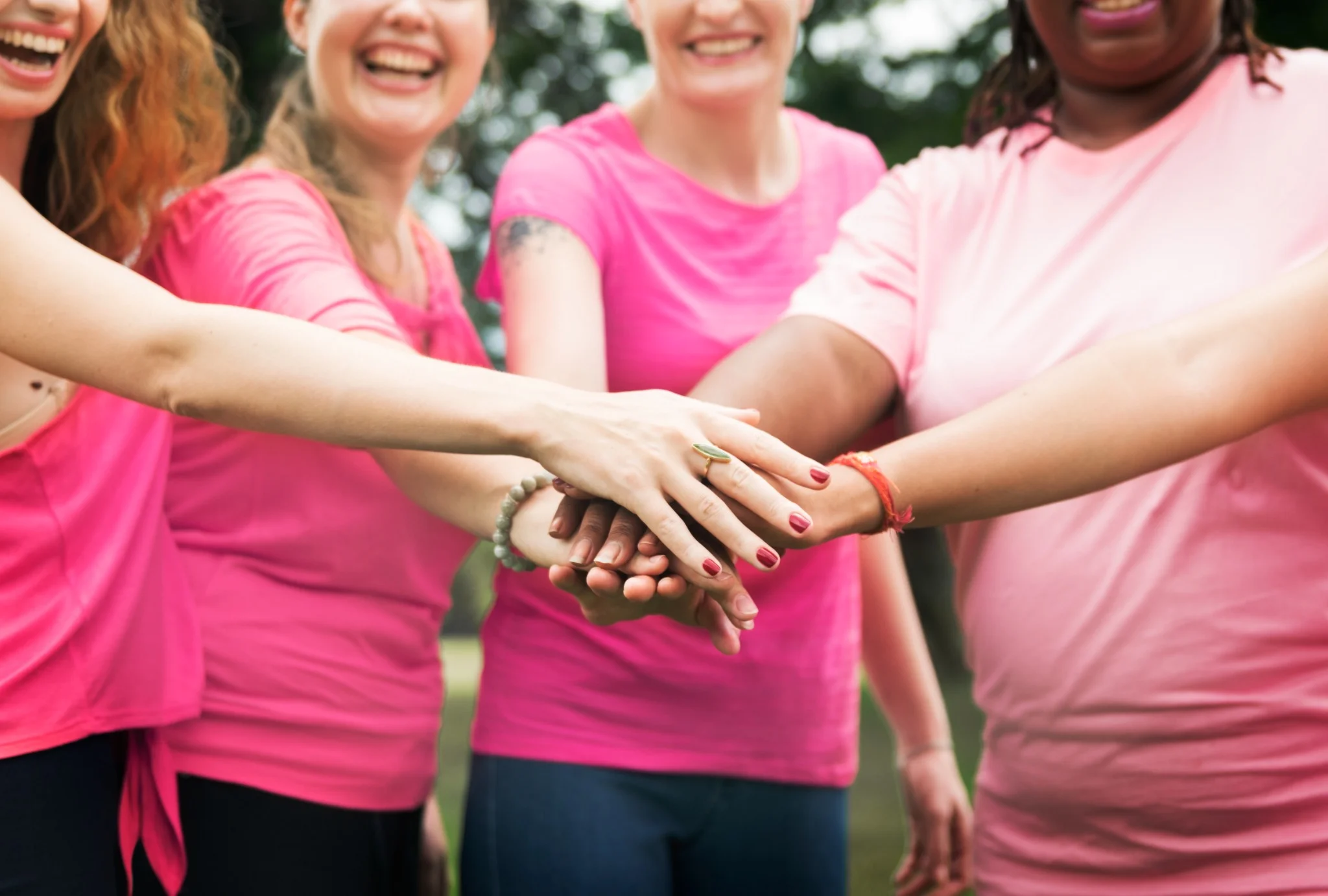 Mulheres unidas pelo Outubro Rosa, mãos sobrepostas em apoio à saúde da mulher, com foco em serviços itinerantes de mamografia e outros exames.
