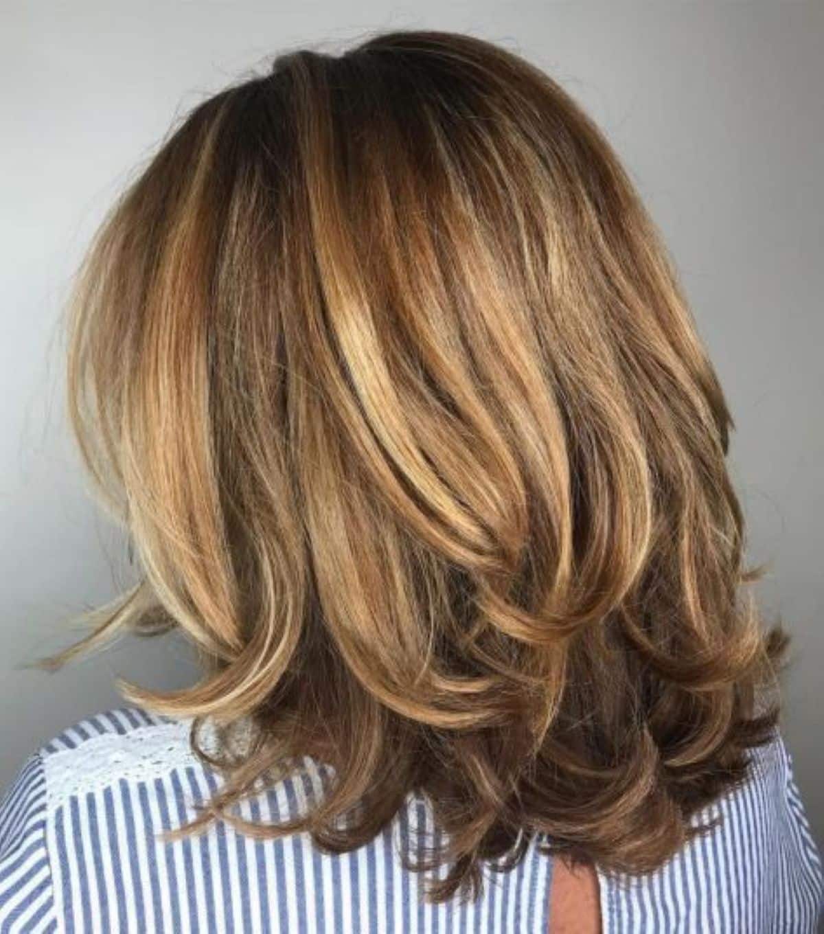 Cabelo médio em camadas suaves, com mechas claras e escuras, adicionando volume e movimento.