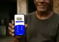 Homem mostrando celular com tela do Programa Bolsa Família Brasil com opções de acesso e informações