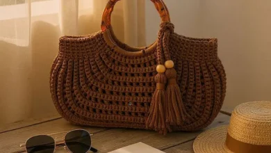 Bolsa de crochê com alça de bambu sobre mesa de madeira, com óculos de sol, chapéu e caderno.