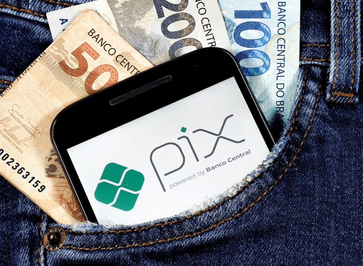 Celular com logo do PIX no bolso de calça junto a notas de real.
