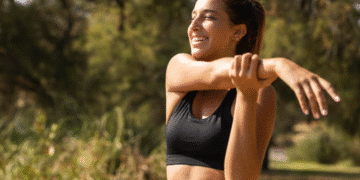 Mulher sorridente e energizada se alongando em uma paisagem verde ao ar livre. A imagem simboliza a energia e o bem-estar controlados pela neuroplasticidade e pelos hormônios.