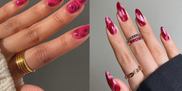 Duas mãos com unhas stiletto alongadas em tons de rosa e vermelho, apresentando a nail art em efeito mármore e rosas.