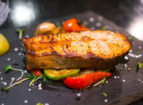 Filé de salmão grelhado acompanhado de legumes coloridos sobre prato preto