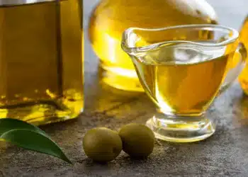 Garrafas e vasilha de azeite de oliva com azeitonas em uma superfície de pedra.