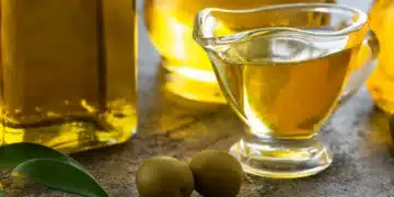 Garrafas e vasilha de azeite de oliva com azeitonas em uma superfície de pedra.