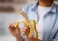 Pessoa segurando uma banana parcialmente descascada, simbolizando o momento ideal para consumir a fruta e obter seus benefícios.