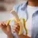 Pessoa segurando uma banana parcialmente descascada, simbolizando o momento ideal para consumir a fruta e obter seus benefícios.