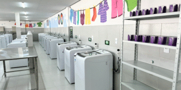 Fileira de máquinas de lavar em lavanderia pública, ilustrando o apoio do governo para reduzir a sobrecarga de trabalho feminino.