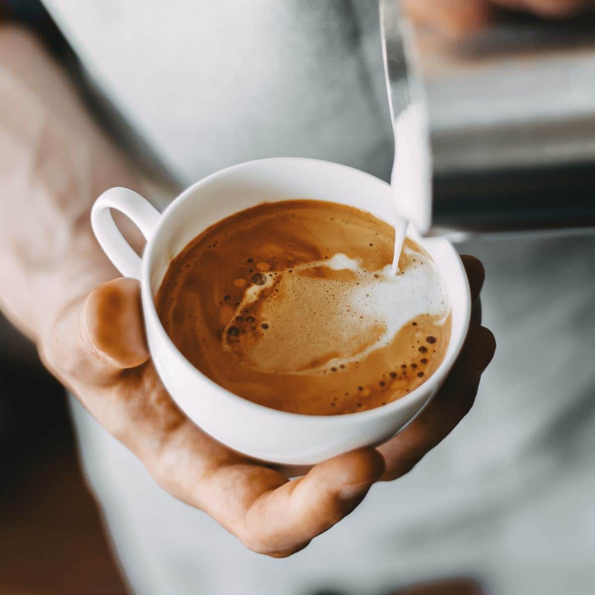 Barista preparando um cappuccino em xícara branca com espuma de leite cremosa