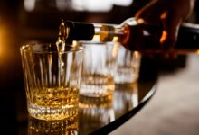 Barman servindo uma dose de bebida alcoólica em copo de cristal, ilustrando o consumo e a discussão sobre o risco de metanol.