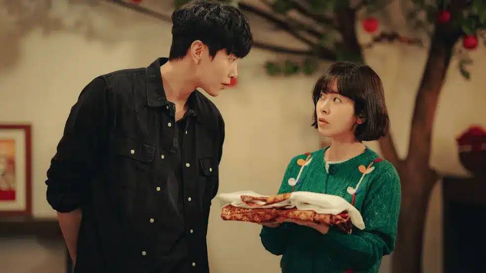 Dorama Behind Your Touch - Netflix Casal de dorama em cena interna, com a personagem feminina segurando um objeto e o personagem masculino observando-a. A imagem representa o mistério e a comédia da série "Behind Your Touch" da Netflix.