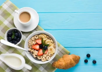 Café da manhã saudável com cereal, frutas frescas, croissant e café sobre mesa azul clara