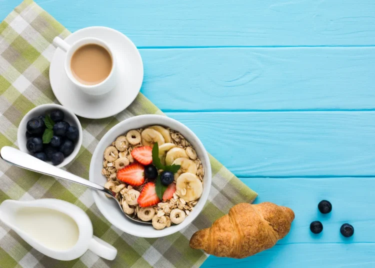 Café da manhã saudável com cereal, frutas frescas, croissant e café sobre mesa azul clara