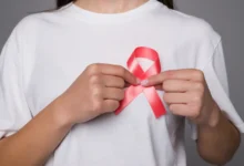 Mulher segurando um laço rosa, símbolo da luta contra o câncer de mama, em uma camiseta branca.