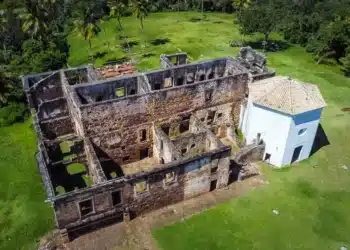 Ruínas do castelo medieval escondido no Brasil, com uma igreja ao lado, em um cenário verdejante.