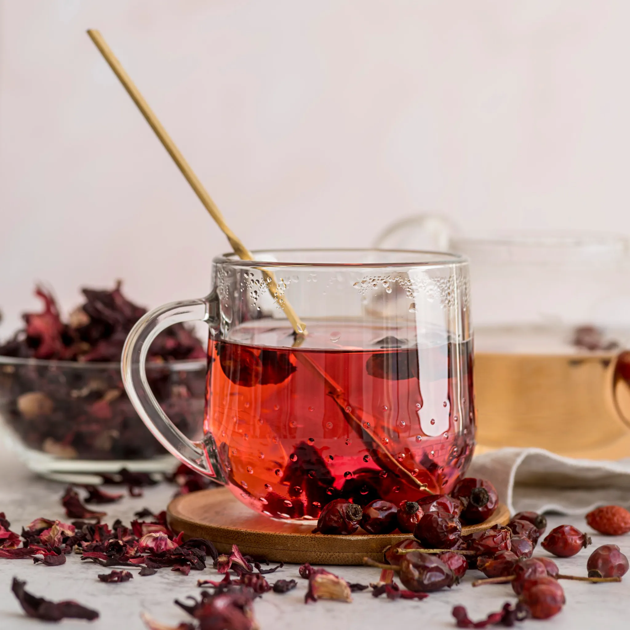 Xícara de chá de hibisco quente, rodeada por flores secas de hibisco e frutas, bebida conhecida por auxiliar na perda de peso e eliminar toxinas.