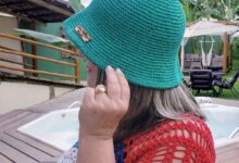 Mulher usando chapéu bucket de crochê verde vibrante, em ambiente externo com banheira de hidromassagem e folhagem tropical ao fundo. Acessório de moda sustentável feito à mão, ideal para o verão.