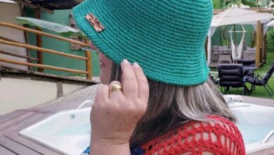 Mulher usando chapéu bucket de crochê verde vibrante, em ambiente externo com banheira de hidromassagem e folhagem tropical ao fundo. Acessório de moda sustentável feito à mão, ideal para o verão.