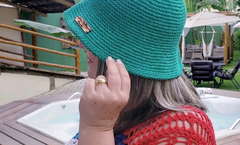 Mulher usando chapéu bucket de crochê verde vibrante, em ambiente externo com banheira de hidromassagem e folhagem tropical ao fundo. Acessório de moda sustentável feito à mão, ideal para o verão.