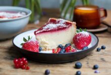 Fatia de cheesecake com calda de frutas vermelhas e morangos, representando uma receita de sobremesa com morangos.