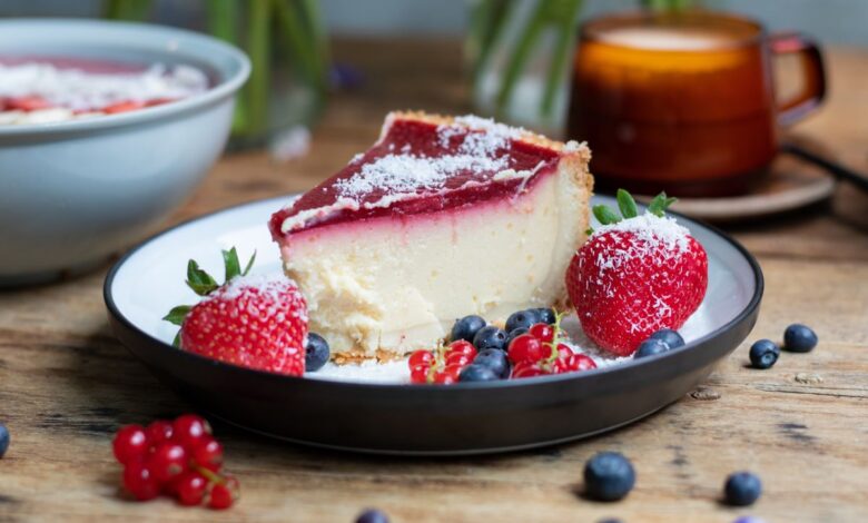 Fatia de cheesecake com calda de frutas vermelhas e morangos, representando uma receita de sobremesa com morangos.