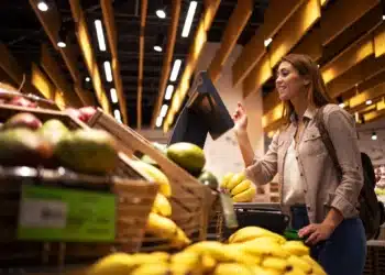 Mulher fazendo compras no supermercado e utilizando balança digital para pesar frutas frescas