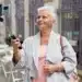 Mulher mais velha sorrindo enquanto usa um selfie stick para tirar uma foto em um ambiente urbano.