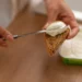 Pessoa espalhando cream cheese caseiro com iogurte natural sobre uma fatia de pão.