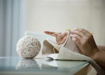 Mulher trabalhando com crochê, utilizando fio metálico, criando uma peça artesanal com brilho discreto.
