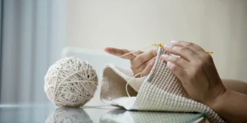 Mulher trabalhando com crochê, utilizando fio metálico, criando uma peça artesanal com brilho discreto.