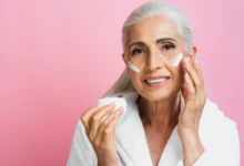 Mulher madura aplicando creme facial em sua pele, destacando os cuidados com a pele após os 50 anos.