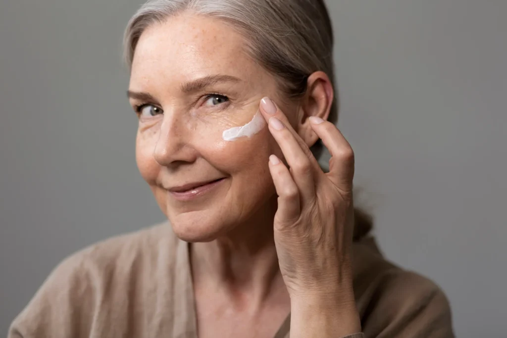 Mulher de 50 anos aplicando creme na pele para manter a saúde e o brilho da pele.