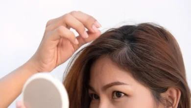 Mulher analisando os fios brancos no cabelo com um espelho de mão.