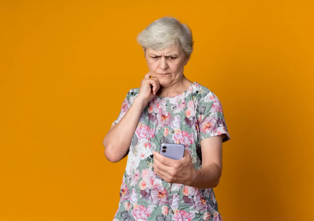 Idosa com expressão desconfiada olhando para o celular, simbolizando atenção a golpes digitais.