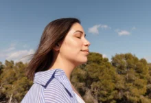Mulher relaxando ao ar livre com os olhos fechados, curtindo um momento de paz e bem-estar, inspirado em hábitos que transformam o humor em minutos.