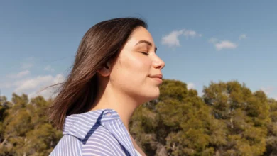 Mulher relaxando ao ar livre com os olhos fechados, curtindo um momento de paz e bem-estar, inspirado em hábitos que transformam o humor em minutos.