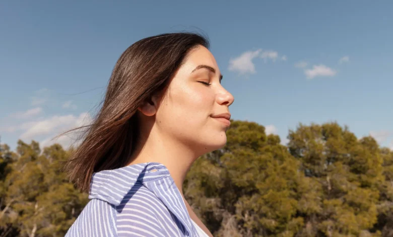 Mulher relaxando ao ar livre com os olhos fechados, curtindo um momento de paz e bem-estar, inspirado em hábitos que transformam o humor em minutos.