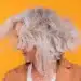 Mulher com cabelo grisalho e volumoso, mostrando movimento com o vento.