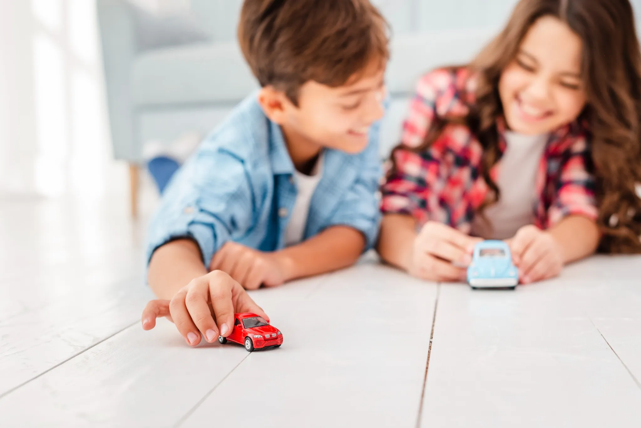 Crianças brincando com carros de brinquedo no chão, recriando aventuras inspiradas em séries de TV como Comandos em Ação e Trombada.