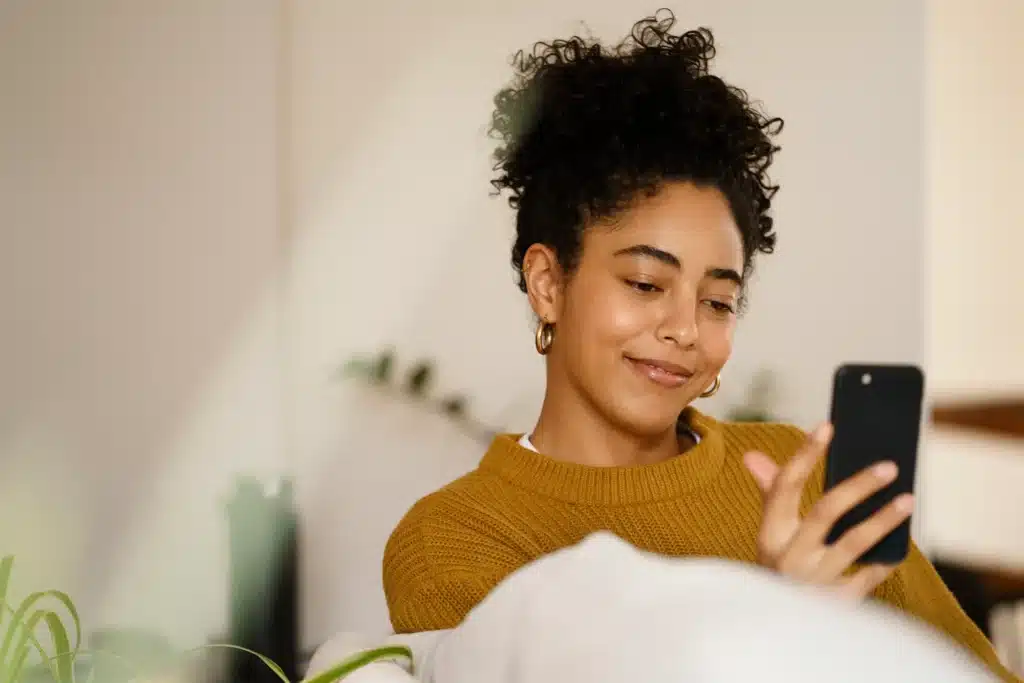 Mensagem Mulher sorrindo enquanto usa smartphone, desejando boas vibrações para os amigos no WhatsApp.