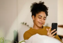 Mulher sorrindo enquanto usa smartphone, desejando boas vibrações para outubro aos amigos no WhatsApp.