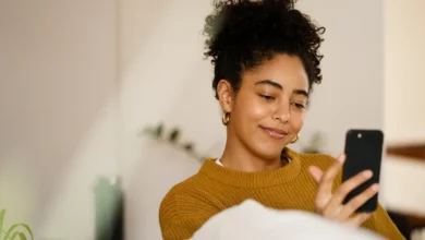 Mulher sorrindo enquanto usa smartphone, desejando boas vibrações para outubro aos amigos no WhatsApp.