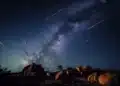 Chuva de meteoros Orionídeas iluminando o céu estrelado com a Via Láctea ao fundo em um cenário rochoso.