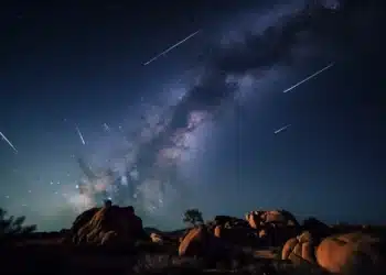 Chuva de meteoros Orionídeas iluminando o céu estrelado com a Via Láctea ao fundo em um cenário rochoso.