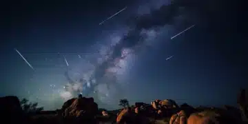 Chuva de meteoros Orionídeas iluminando o céu estrelado com a Via Láctea ao fundo em um cenário rochoso.